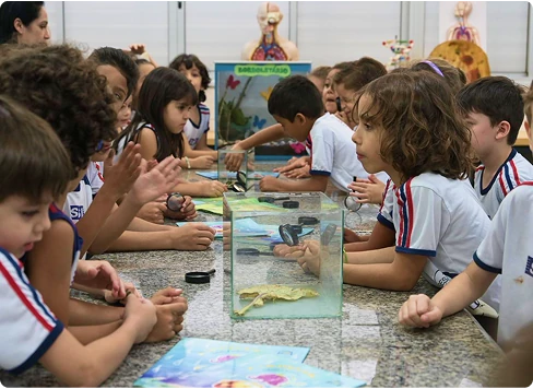 Técnico do SENAI opera um microscópio eletrônico em um laboratório, analisando imagens em dois monitores à sua frente.