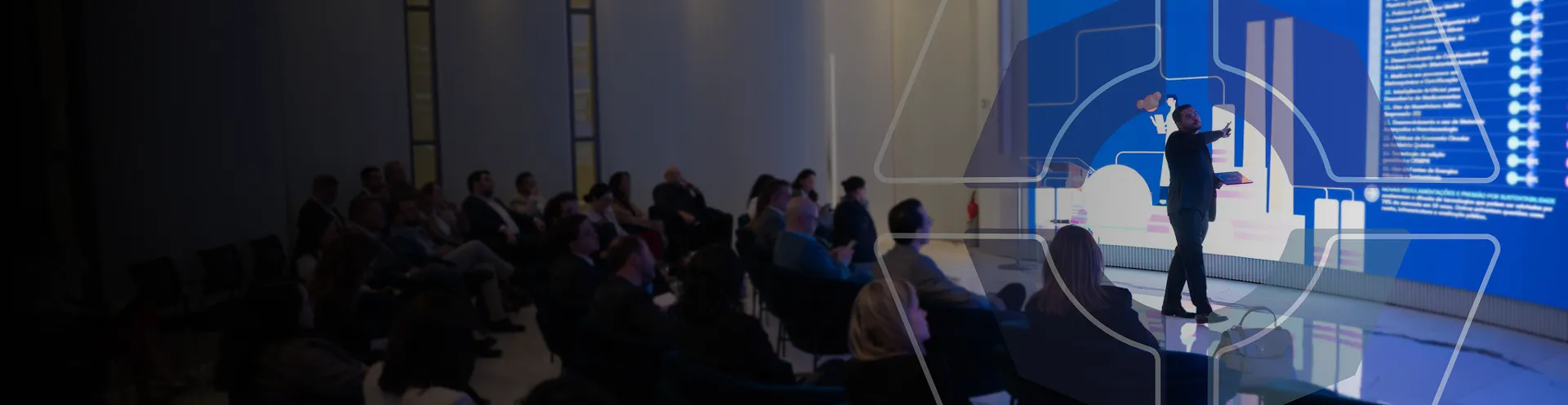 Homem no palco fazendo palestra para dezenas de pessoas.