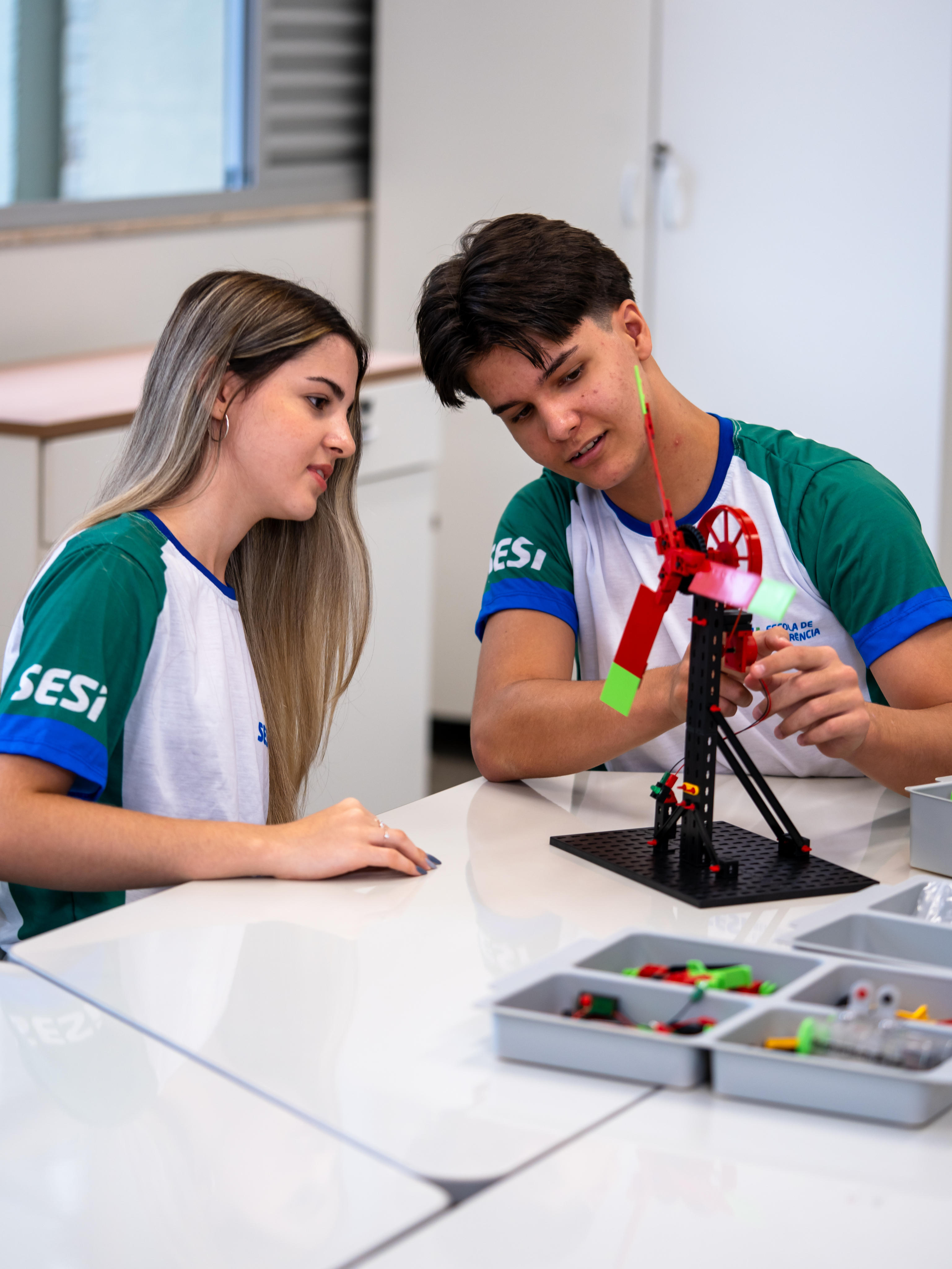 Dois jovens conversam e observam um protótipo de cata-vento.